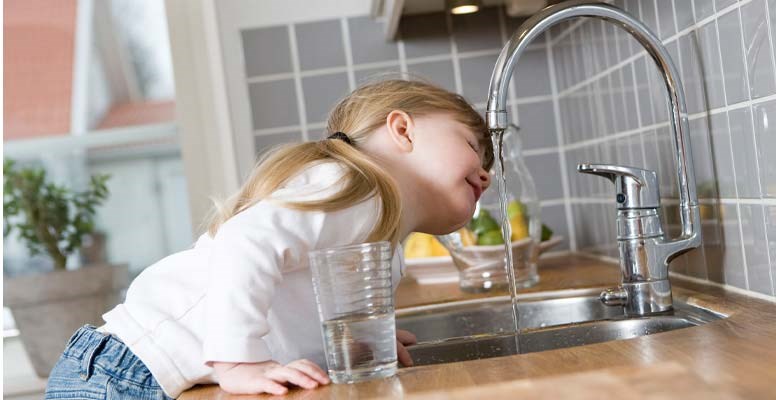 Little girl drinking water at kitchen sink