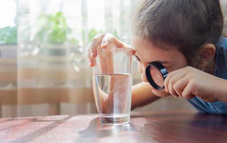 Kid looking into glass of water with particles